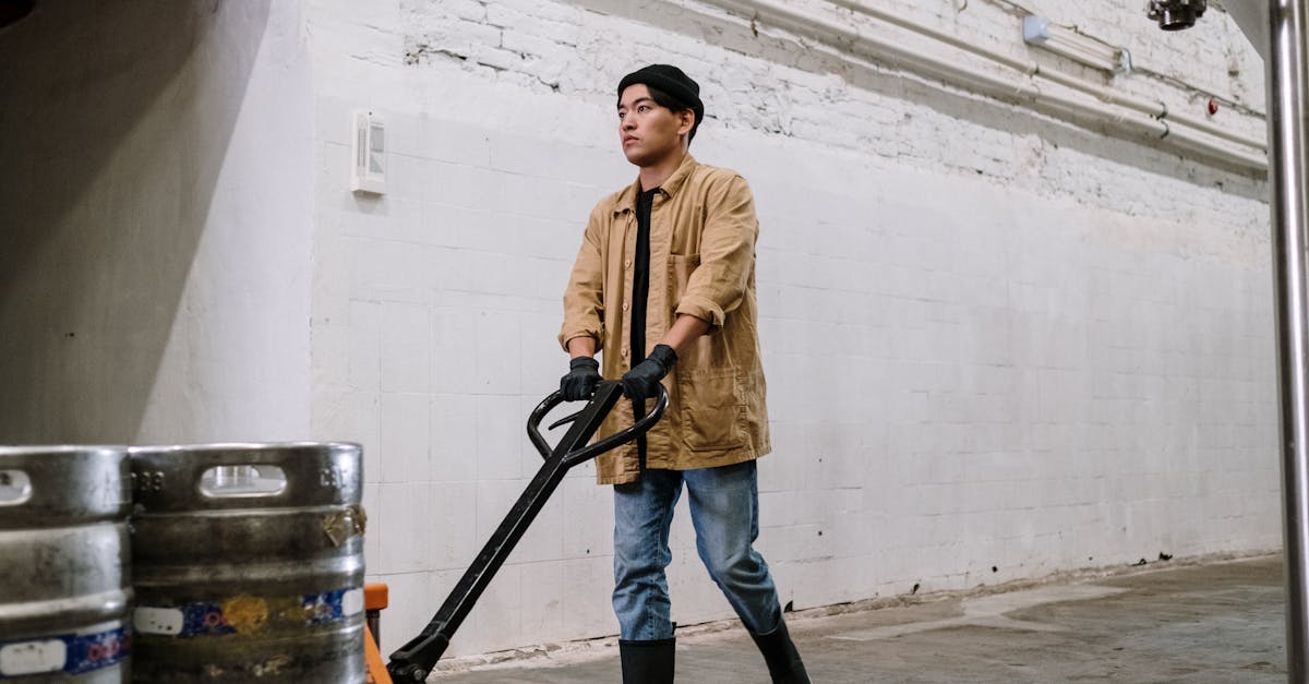 Young man in brewery moving barrels with hand truck. Modern industrial setting.